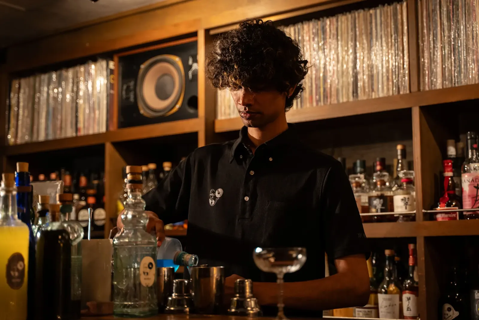 レコード棚とボトルを背に、カウンターでカクテルをつくるバーテンダー
