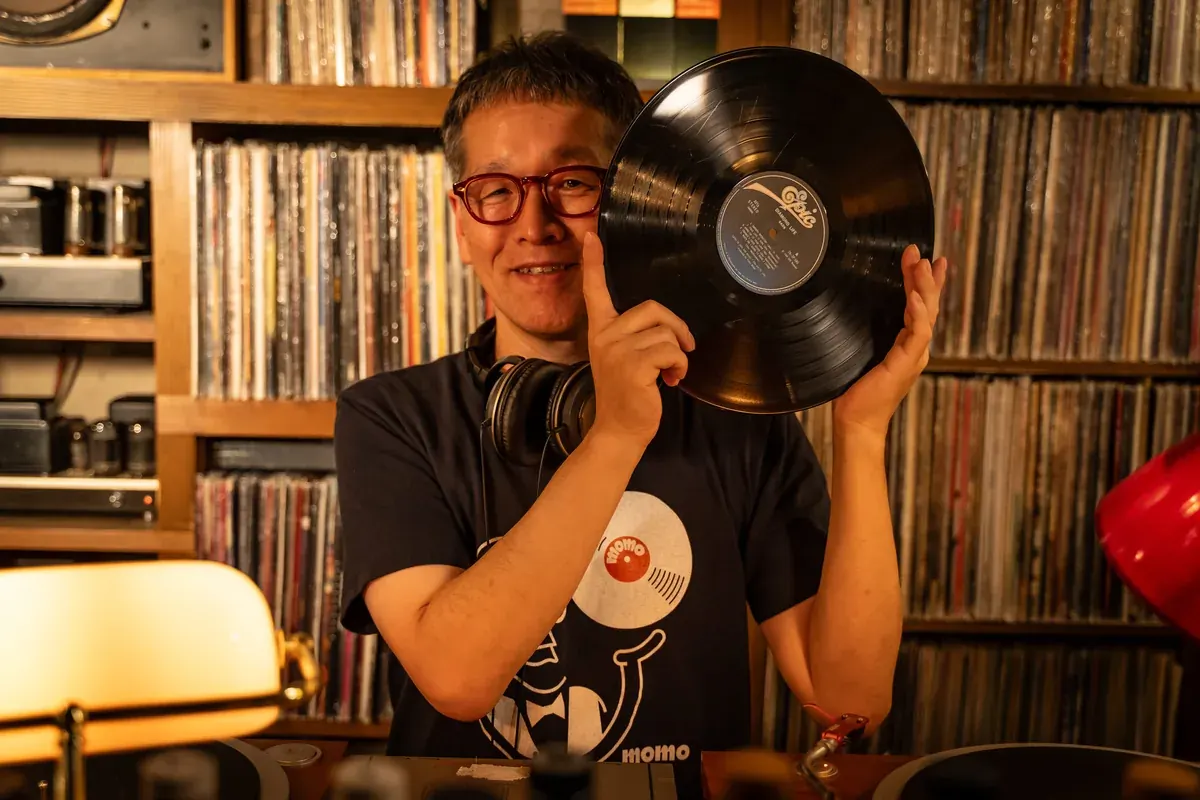 レコード棚の前で、レコードを手に笑顔を見せる店内での一枚